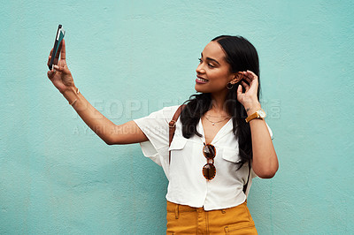 Buy stock photo Cropped shot of an attractive young woman standing and using her cellphone to take a selfie against a blue background