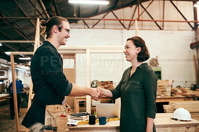Buy stock photo Cropped shot of two young carpenters shaking hands while working together inside their workshop