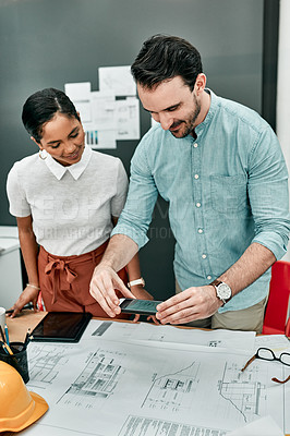Buy stock photo Shot of two architects using a cellphone to take photos of blueprints in an office