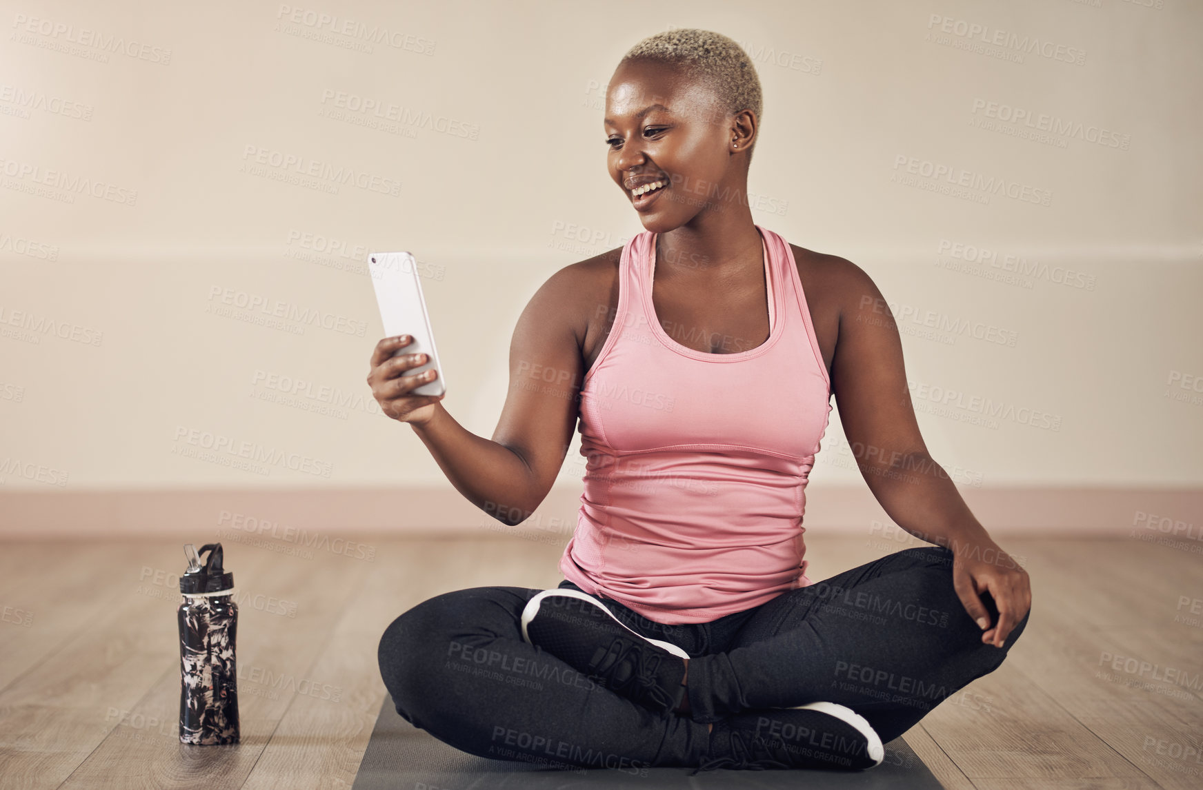 Buy stock photo Full length shot of an attractive young woman sitting alone and using her cellphone after an indoor yoga session