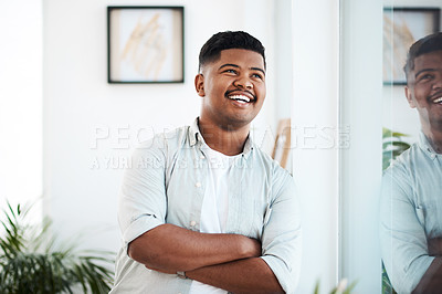 Buy stock photo Shot of a young businessman looking thoughtfully out of a window in a modern office