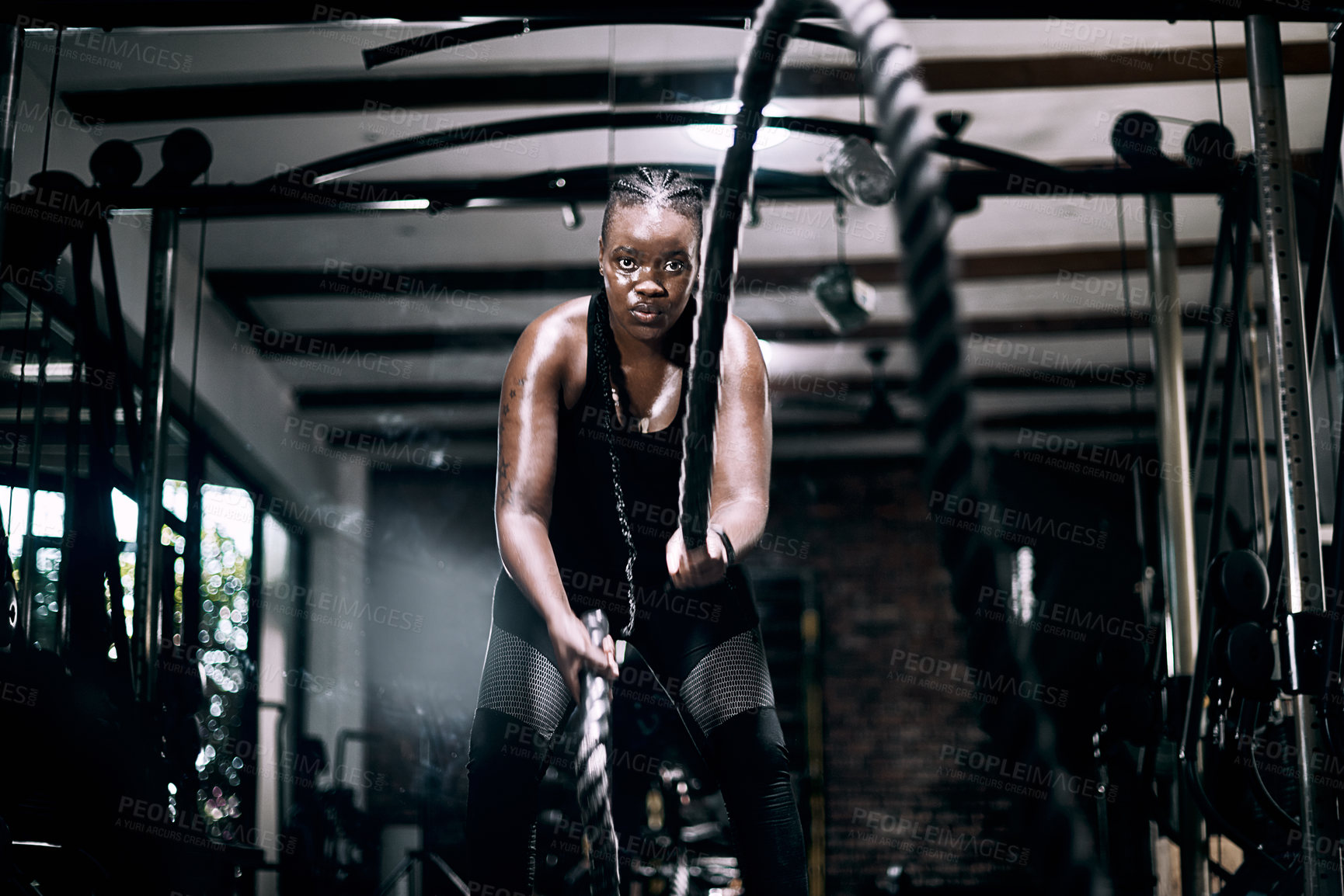Buy stock photo Cropped portrait of an attractive young female athlete working out with battle ropes in the gym