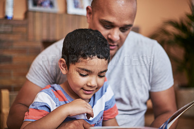 Buy stock photo Cropped shot of a cheerful young man and his son reading a storybook together at home during the day