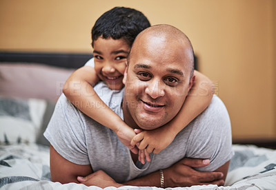 Buy stock photo Portrait of a cheerful little boy hanging on his father's back while hanging out in the bedroom at home during the day