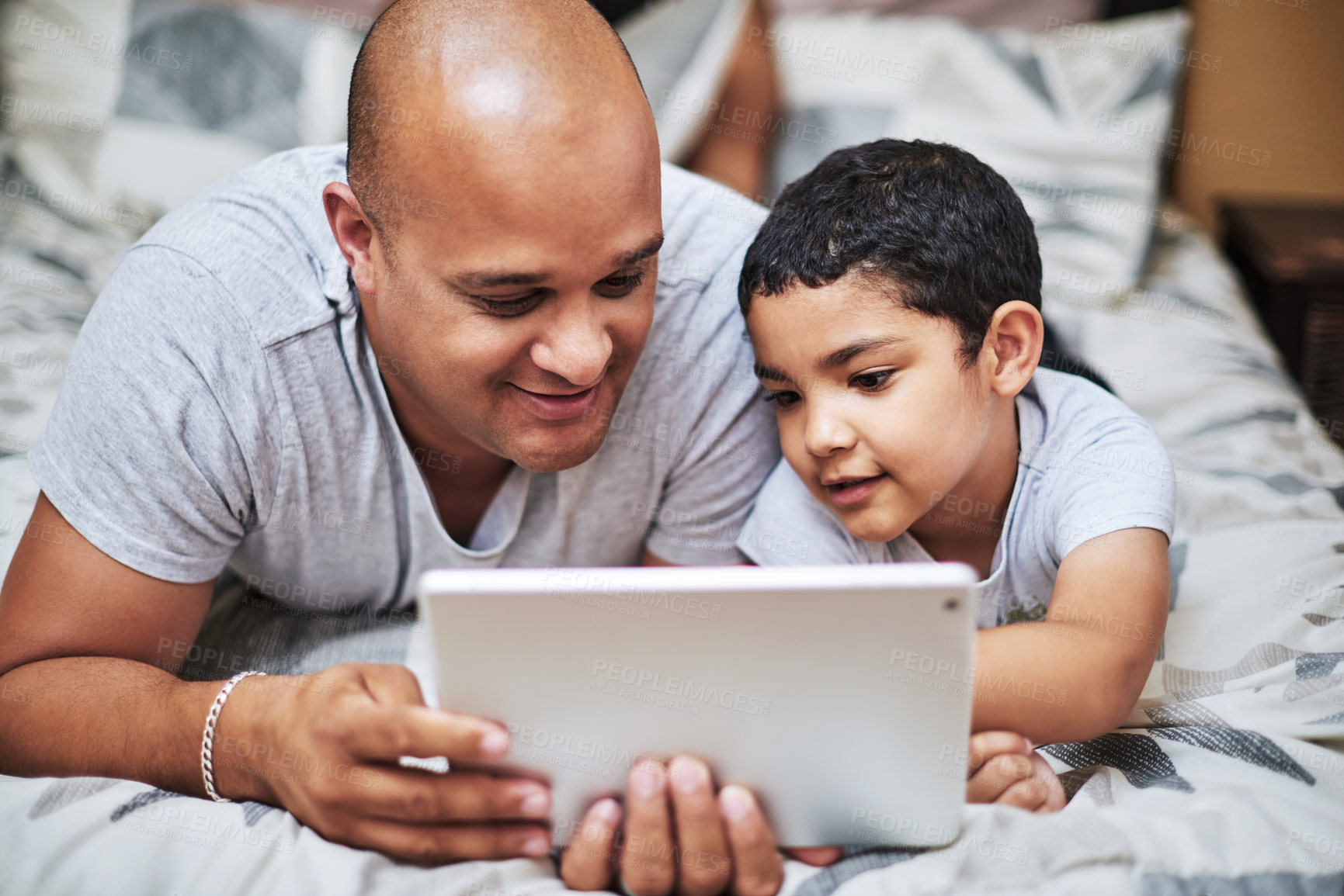 Buy stock photo Cropped shot of a cheerful young man and his son watching videos on a digital tablet together  while hanging out on a bed at home during the day