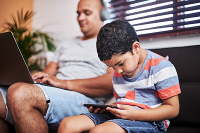 Buy stock photo Cropped shot of a carefree little boy browsing on a digital tablet while his father works on his laptop on the sofa at home during the day