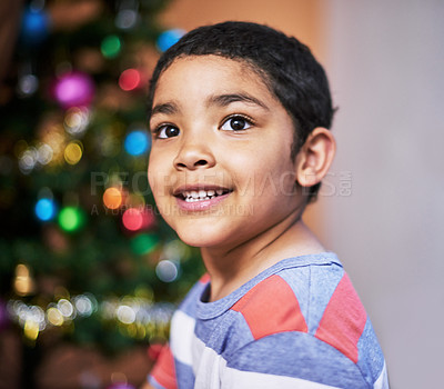 Buy stock photo Cropped shot of a cheerful little boy looking into the distance with a Christmas tree in the background at home during the day