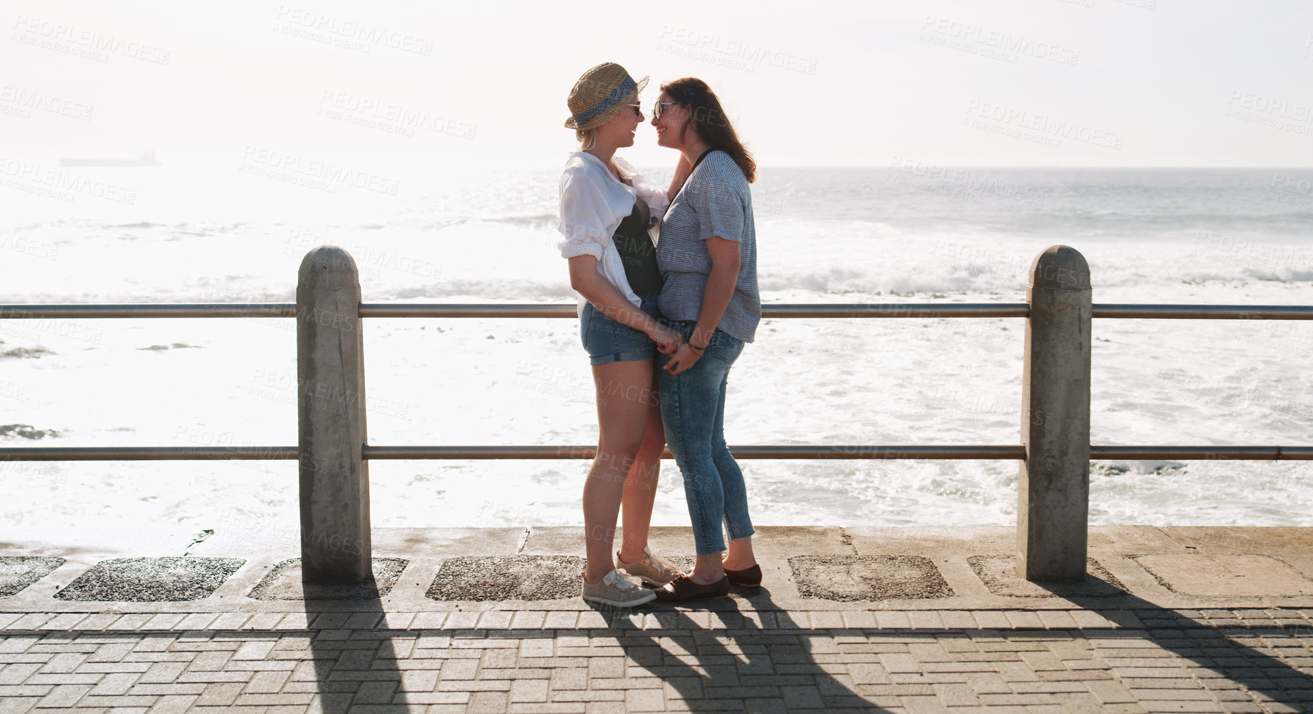 Buy stock photo Full length shot of an affectionate and happy young couple standing together on a promenade near the beach