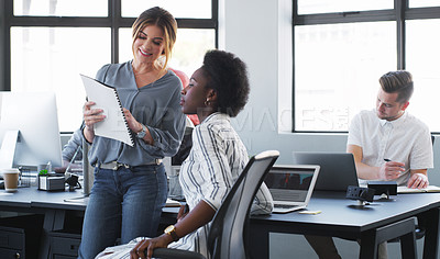 Buy stock photo Shot of two young businesswomen discussing paperwork in a modern office