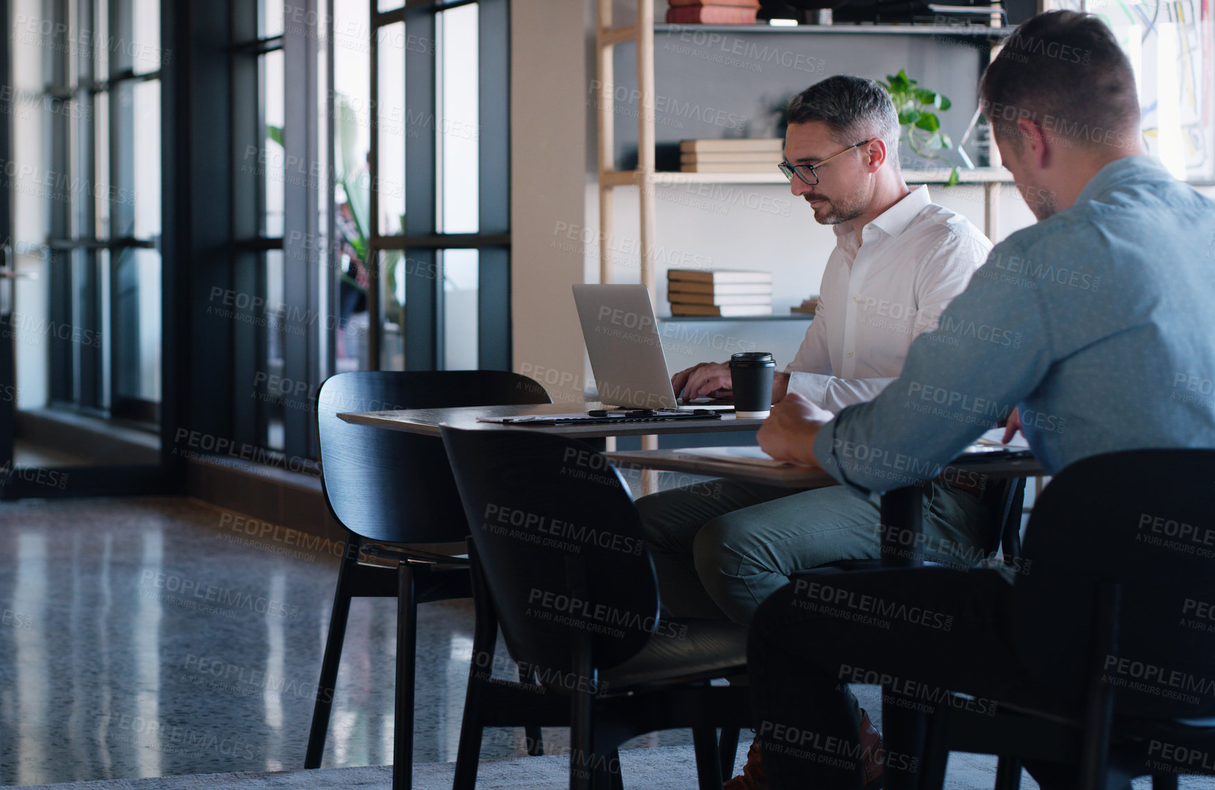 Buy stock photo Shot of two businessmen using their laptops at a desk in a modern office