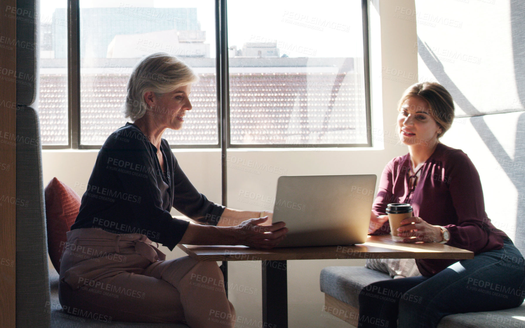 Buy stock photo Shot of two businesswomen using a laptop and having a discussion in a modern office