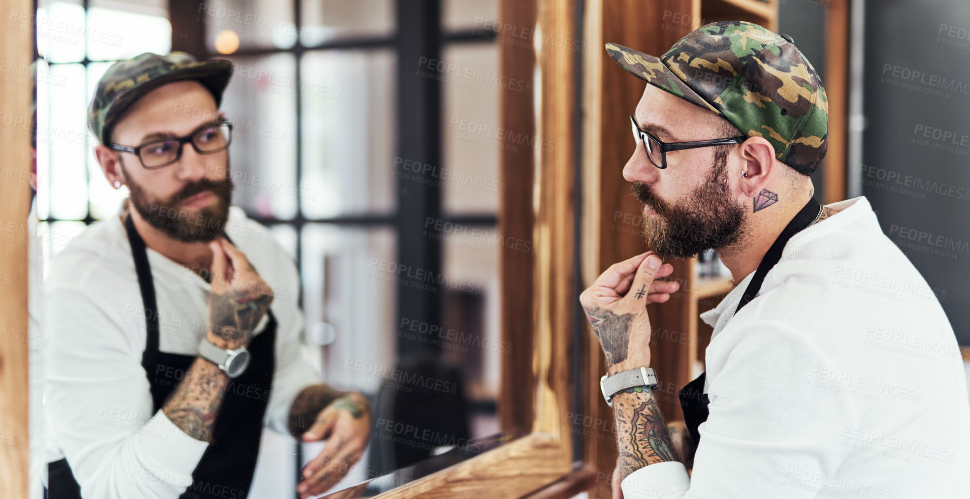 Buy stock photo Shot of a handsome young man looking in the mirror and examining his beard inside a barbershop