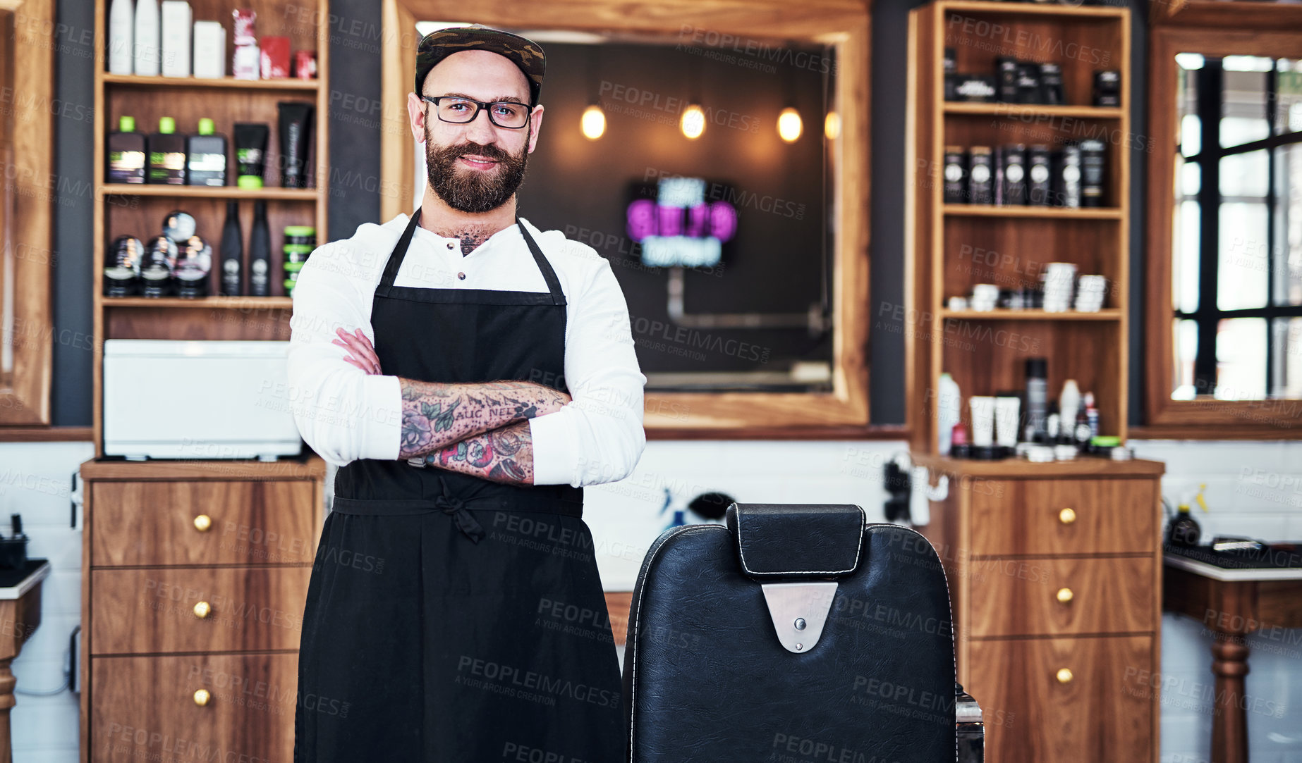 Buy stock photo Portrait of a handsome young barber posing with his arms folded inside a barbershop