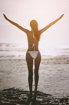 Buy stock photo Rearview shot of an attractive young woman wearing a bikini posing with her arms outstretched at the beach