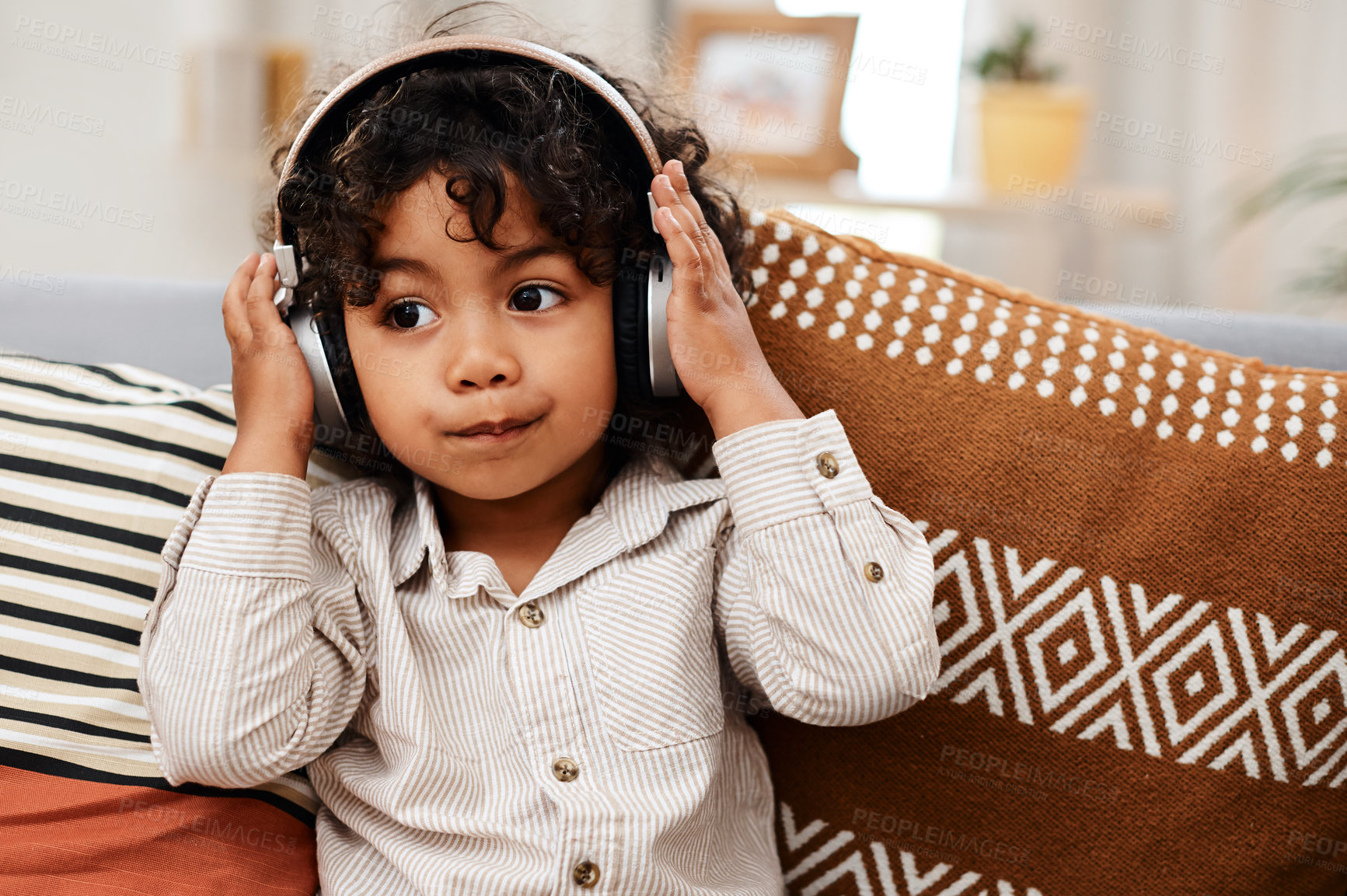Buy stock photo Cropped shot of an adorable little boy listening to music on headphones while sitting on a sofa at home