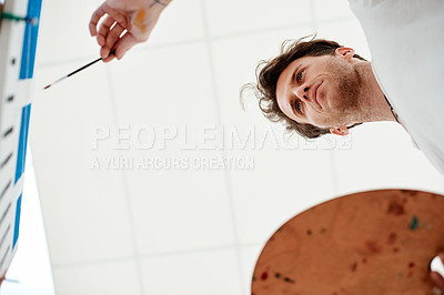 Buy stock photo Low angle shot of a handsome young artist standing alone and painting during an art class in the studio
