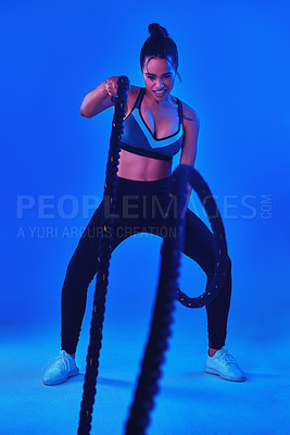 Buy stock photo Full length shot of an attractive young sportswoman working out with battle ropes against a blue background