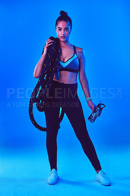 Buy stock photo Full length shot of an attractive young sportswoman posing carrying battle ropes against a blue background