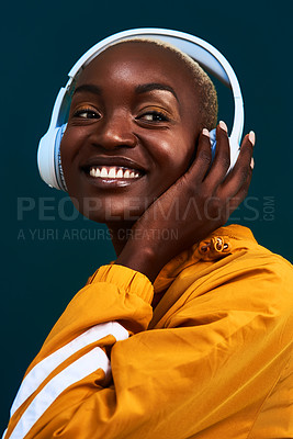 Buy stock photo Cropped shot of an attractive young sportswoman standing alone against a dark background and listening to music through headphones