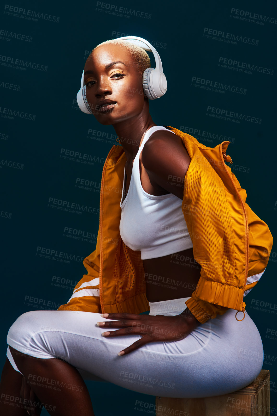 Buy stock photo Cropped portrait of an attractive young sportswoman sitting alone and posing with headphones on against a dark studio background