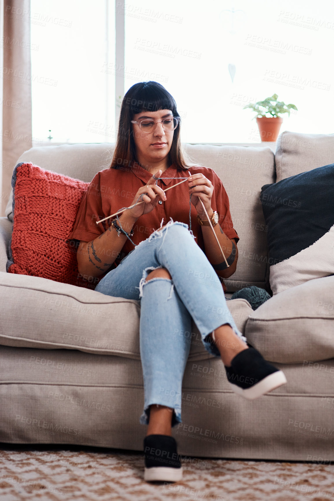 Buy stock photo Full length shot of a young woman knitting while relaxing at home