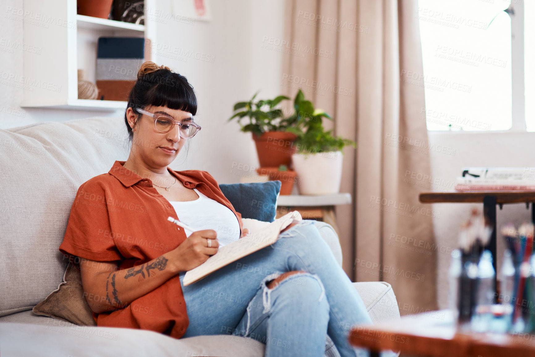 Buy stock photo Shot of an attractive young woman writing while relaxing at home