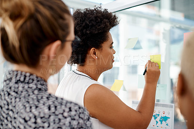 Buy stock photo Rearview shot of a group of businesswomen brainstorming with notes on a glass wall in an office