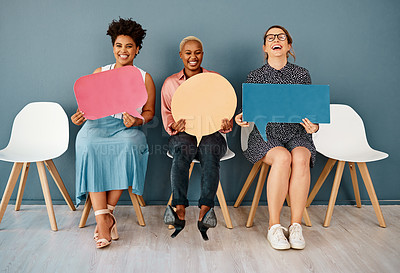 Buy stock photo Studio portrait of a group of attractive young businesswomen holding speech bubbles while sitting in a row against a grey background