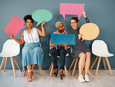 Buy stock photo Studio shot of a group of attractive young businesswomen holding speech bubbles while sitting in a row against a grey background