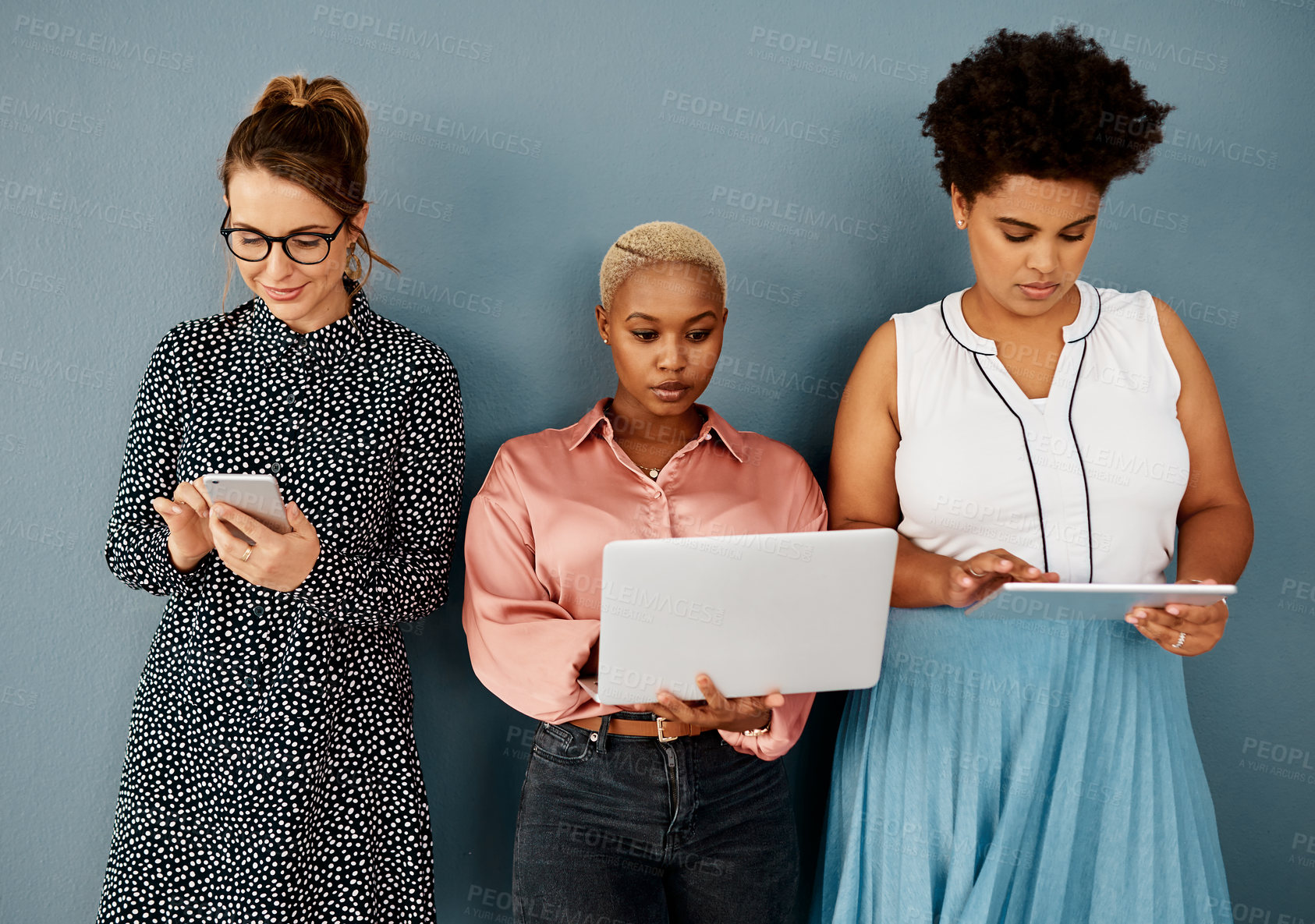 Buy stock photo Studio shot of a group of attractive young businesswomen using wireless technology while standing against a grey background