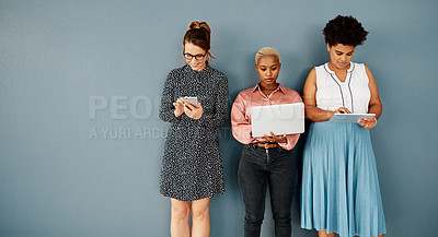 Buy stock photo Studio shot of a group of attractive young businesswomen using wireless technology while standing against a grey background