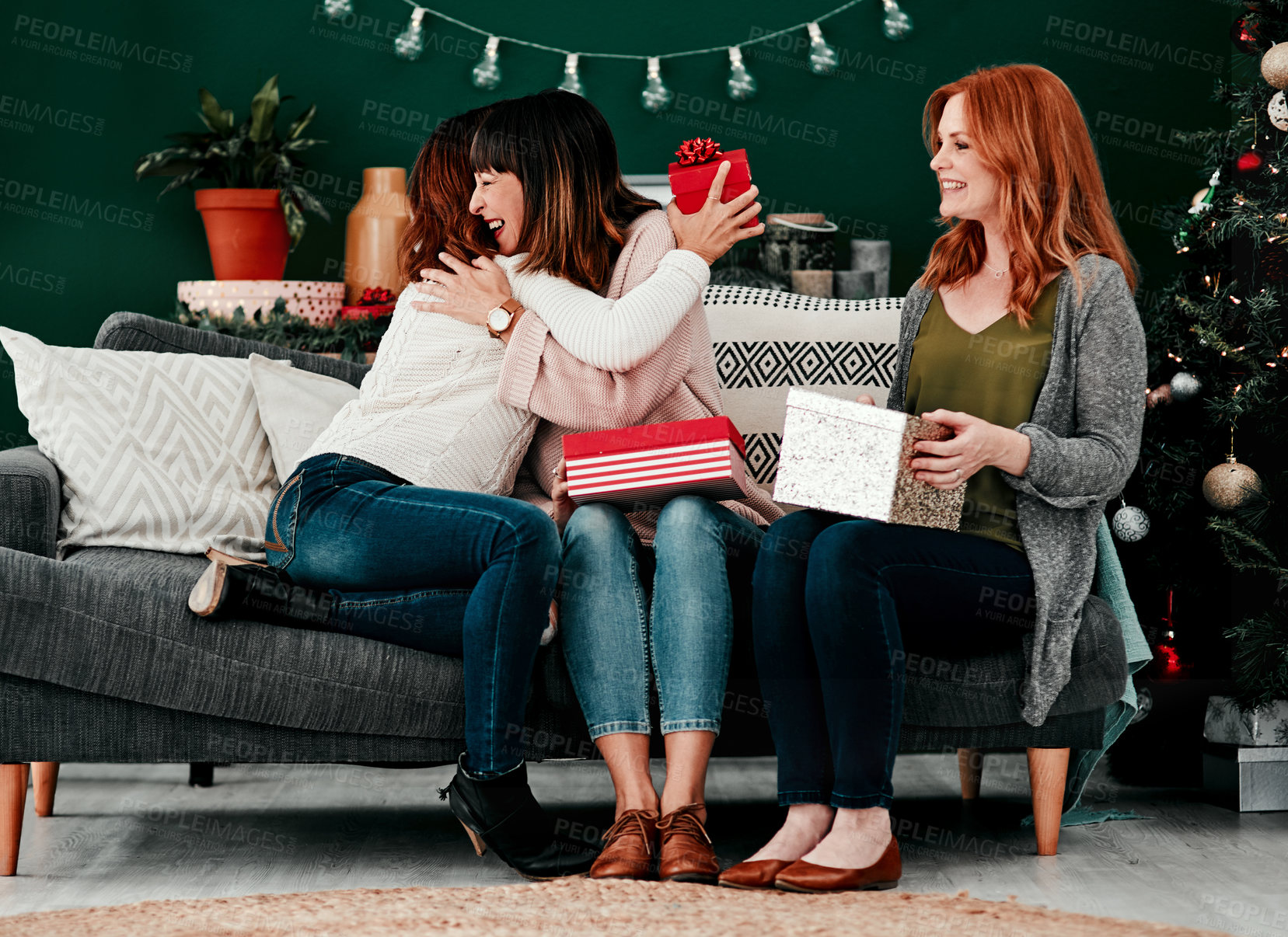 Buy stock photo Shot of three attractive middle aged women opening presents together while being seated on a sofa during Christmas time