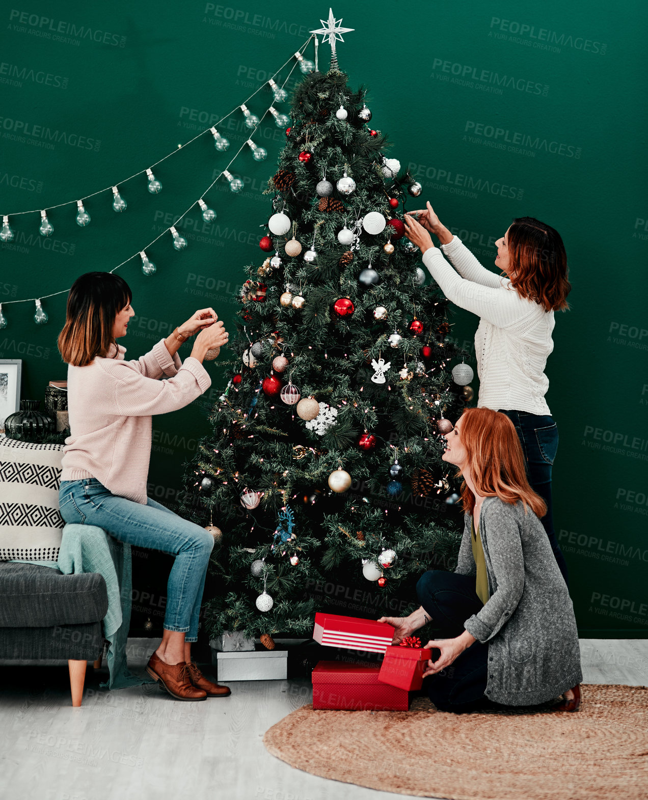 Buy stock photo Shot of three attractive middle aged women decorating a Christmas tree together at home