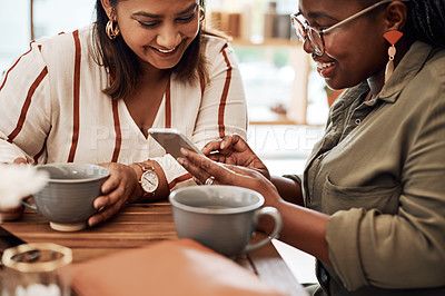 Buy stock photo Shot of two young women using a smartphone together at a cafe