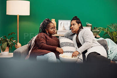 Buy stock photo Shot of two young women having popcorn and chatting on the sofa at home