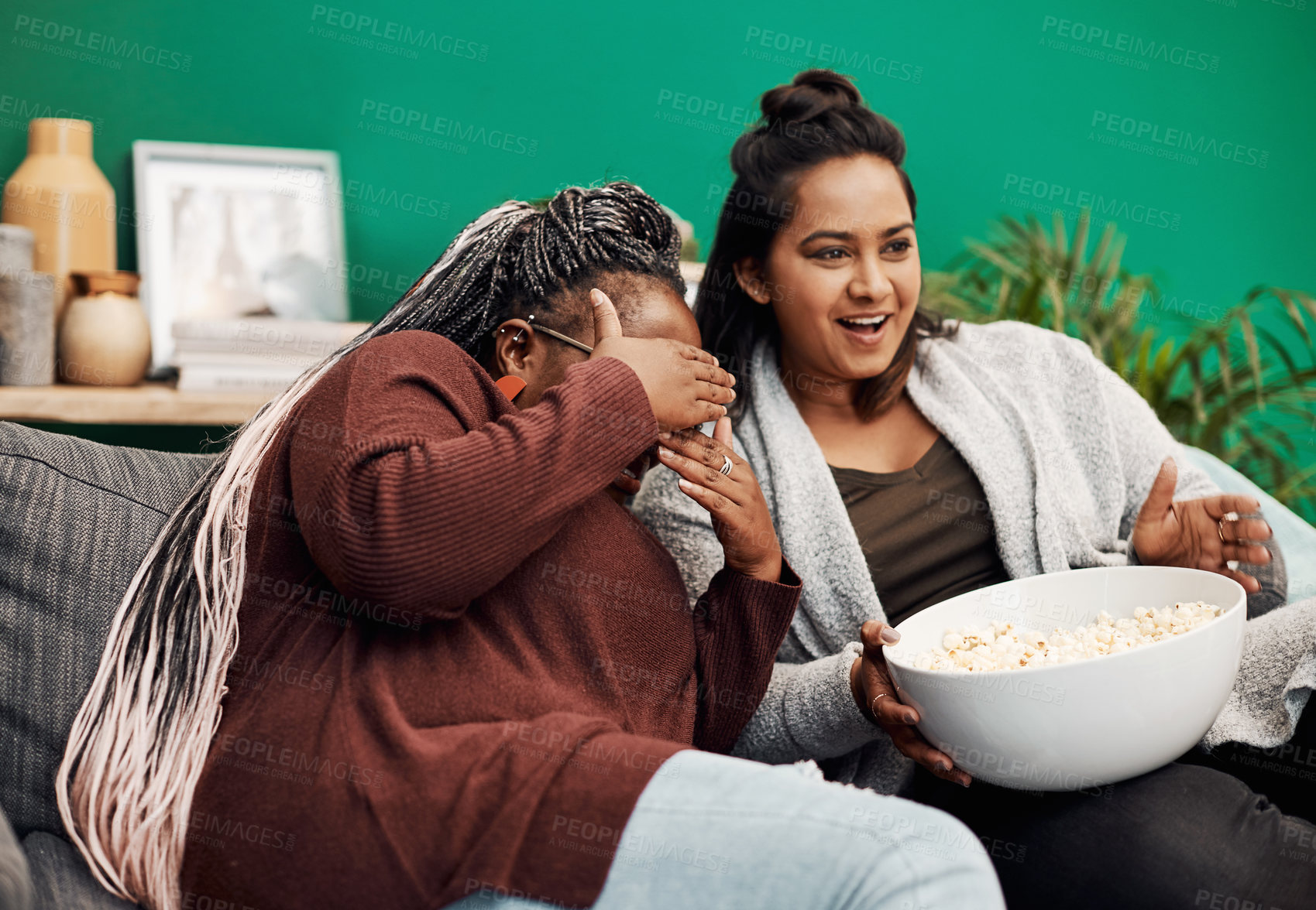 Buy stock photo Shot of two young women having popcorn and watching tv together at home