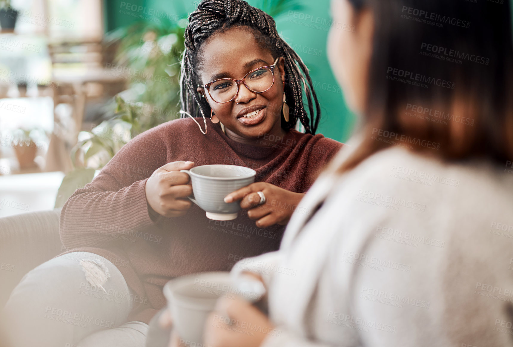 Buy stock photo Shot of two young women having coffee and chatting on the sofa at home