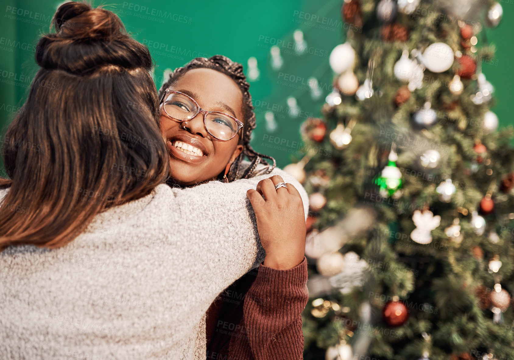Buy stock photo Shot of two happy young women hugging each other during Christmas at home