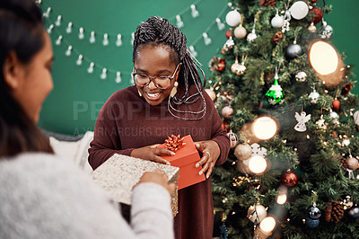 Buy stock photo Shot of two happy young women exchanging gifts during Christmas at home