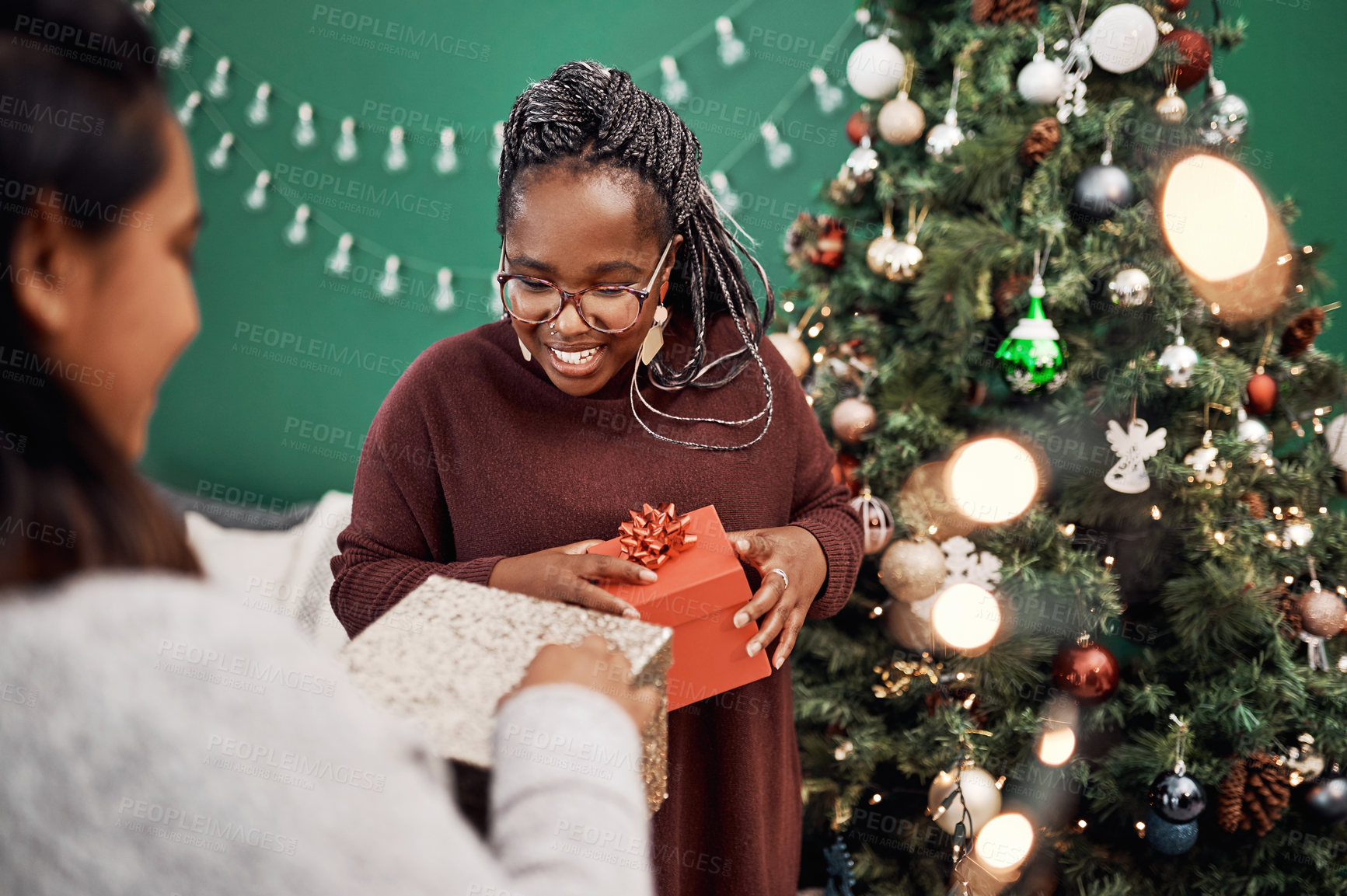 Buy stock photo Shot of two happy young women exchanging gifts during Christmas at home