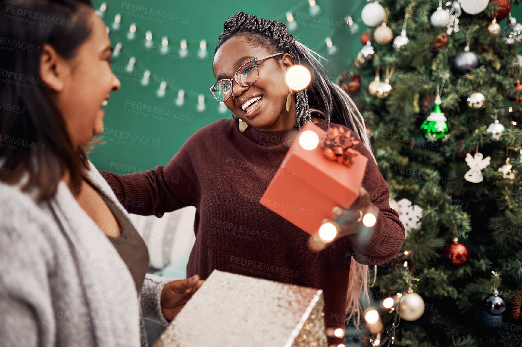 Buy stock photo Shot of two happy young women exchanging gifts during Christmas at home