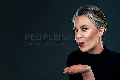Buy stock photo Studio portrait of a beautiful mature woman blowing a kiss against a dark background