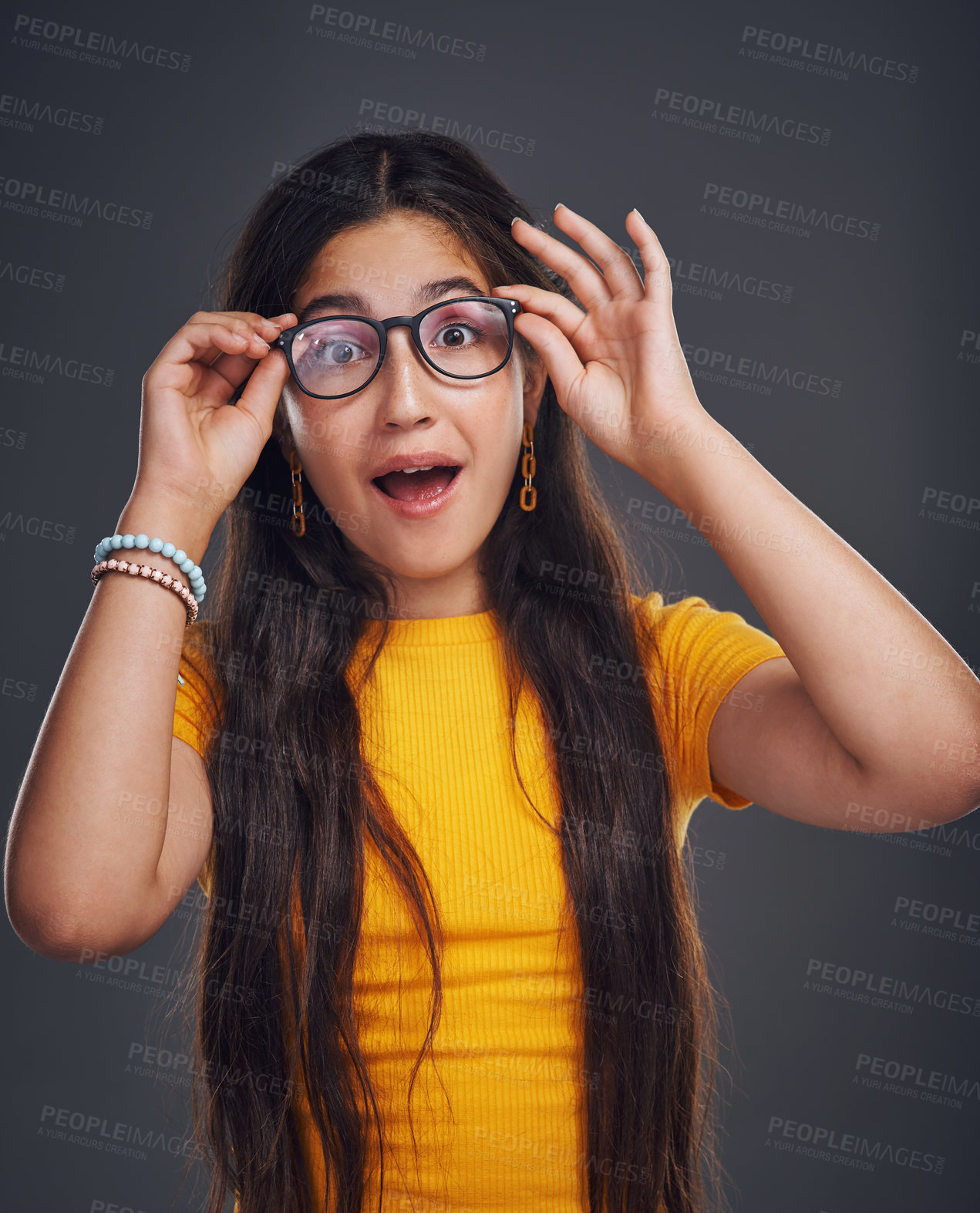 Buy stock photo Cropped portrait of an attractive teenage girl wearing glasses and feeling playful against a dark background in the studio