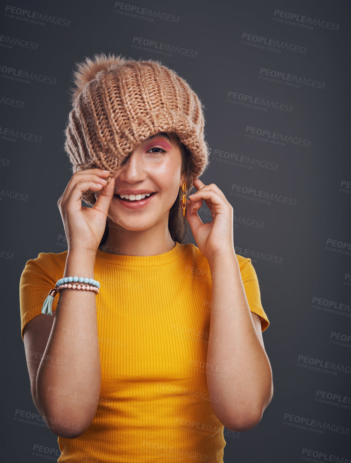 Buy stock photo Cropped portrait of an attractive teenage girl wearing a beanie and feeling playful against a dark studio background