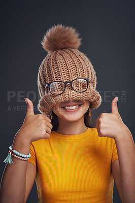 Buy stock photo Smile, hide and girl with beanie in studio with glasses for funny, comic or silly joke with thumbs up. Goofy, happy and woman cover face with knit hat and spectacles for comedy by black background.