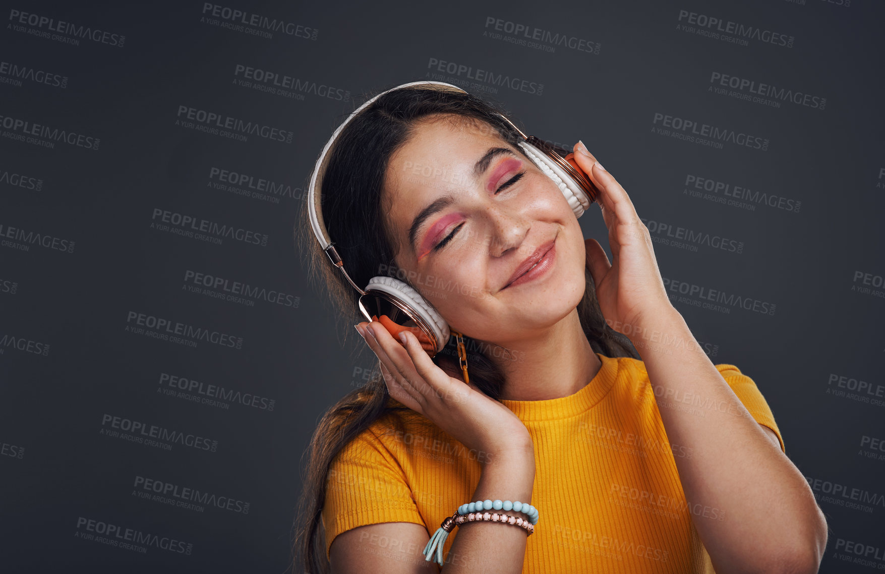Buy stock photo Cropped shot of an attractive teenage girl standing against a dark background alone and listening to music through headphones