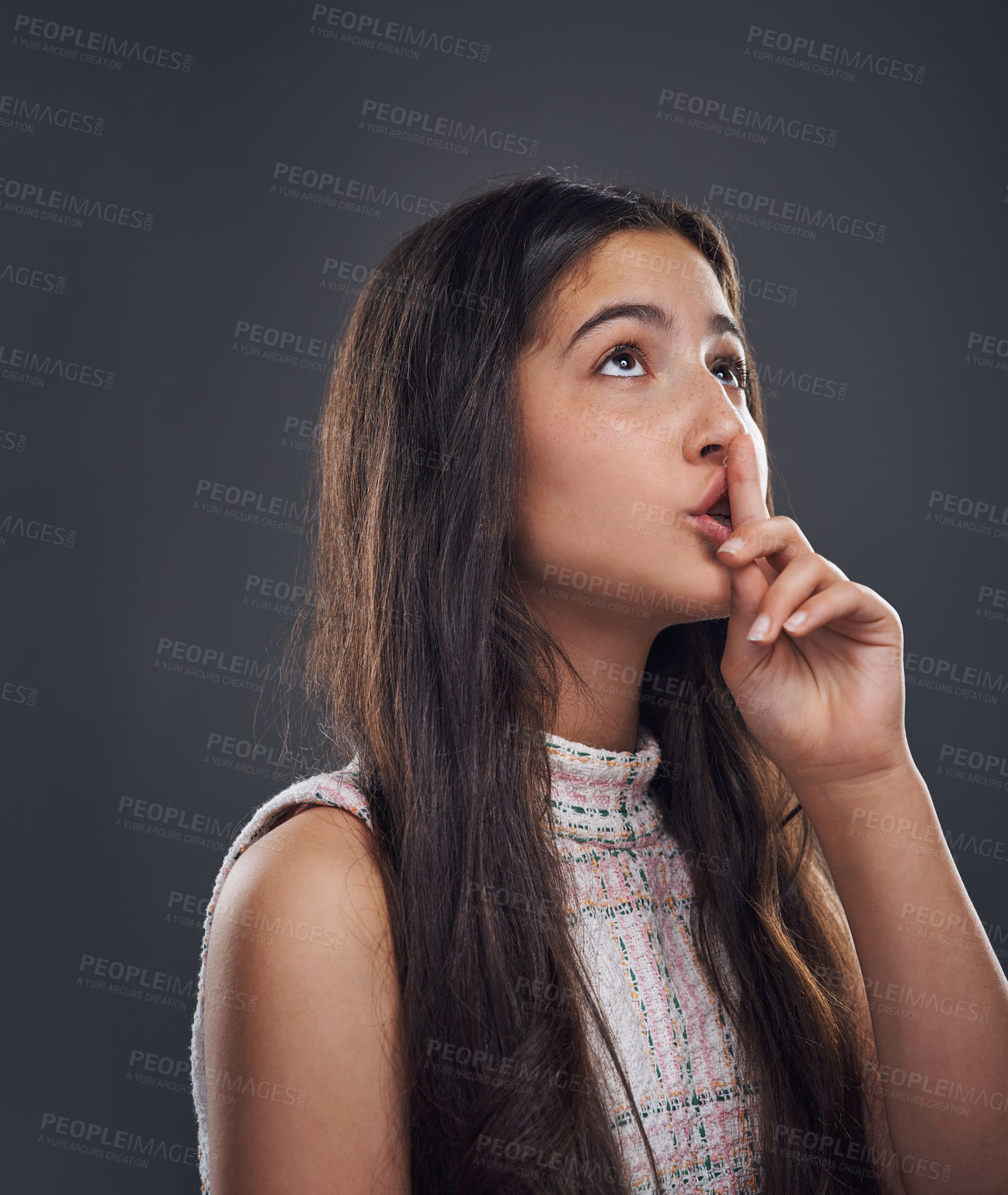 Buy stock photo Cropped shot of an attractive teenage girl standing with her finger to her lips against a dark studio background