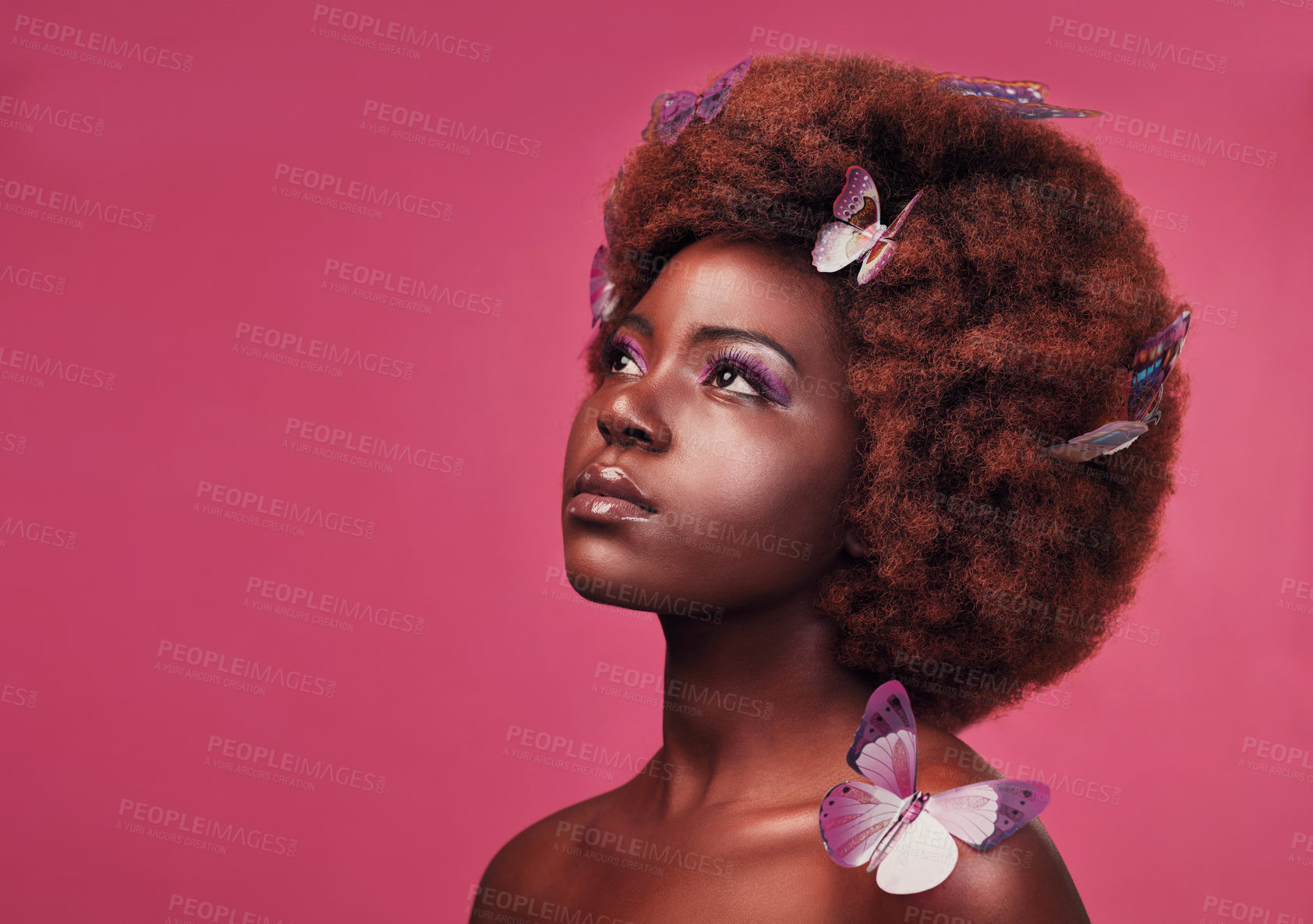 Buy stock photo Creative, cosmetic and woman with butterflies in her hair and a makeup, natural and elegant face. Art, fantasy and young African female model posing with beautiful insects by a pink studio background