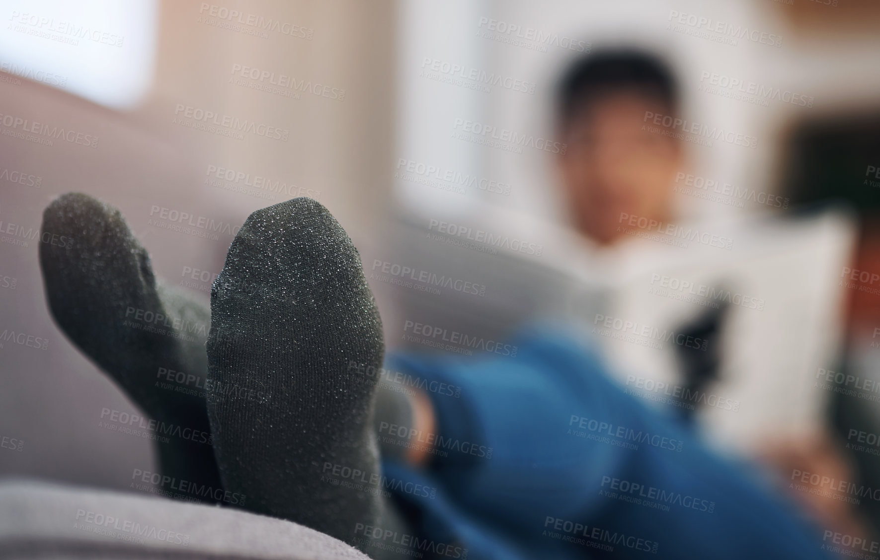 Buy stock photo Cropped shot of an unrecognizable woman sitting alone in her living room with her feet up during a day off