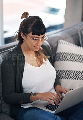 Buy stock photo Cropped shot of an attractive young woman sitting alone in her living room and using her laptop